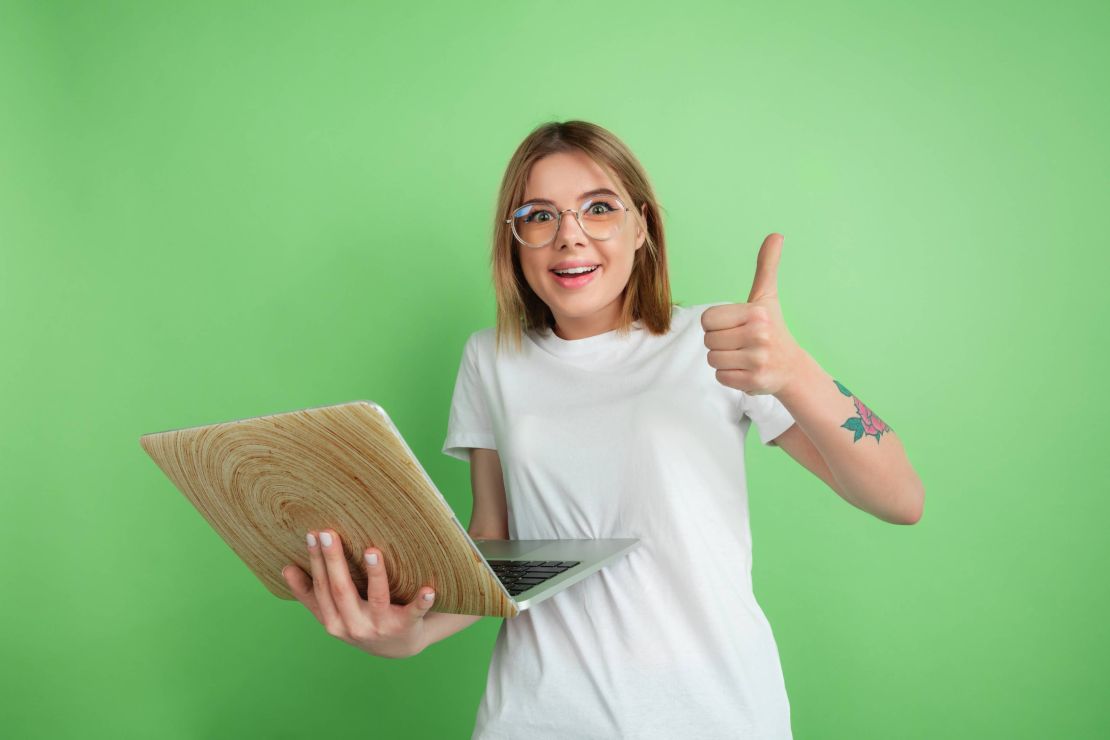 mladá žena pri zelenom pozadí s laptopom v ruke drží palec hore